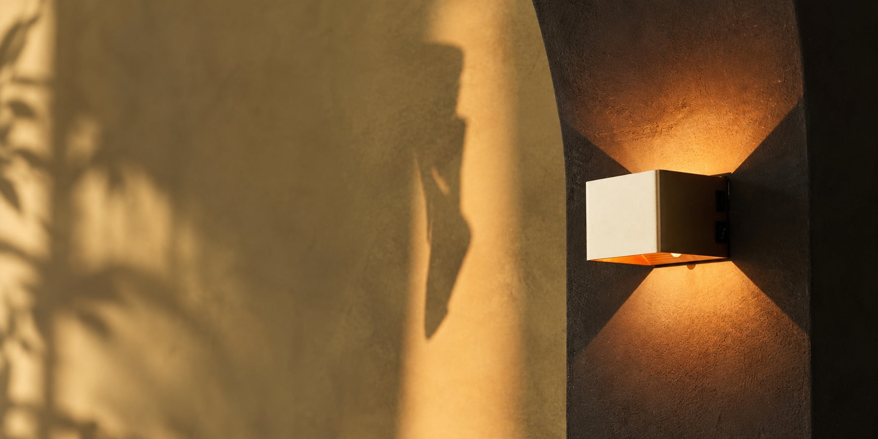 Minimalist rechargeable wall light glowing in warm evening light, mounted without a cable