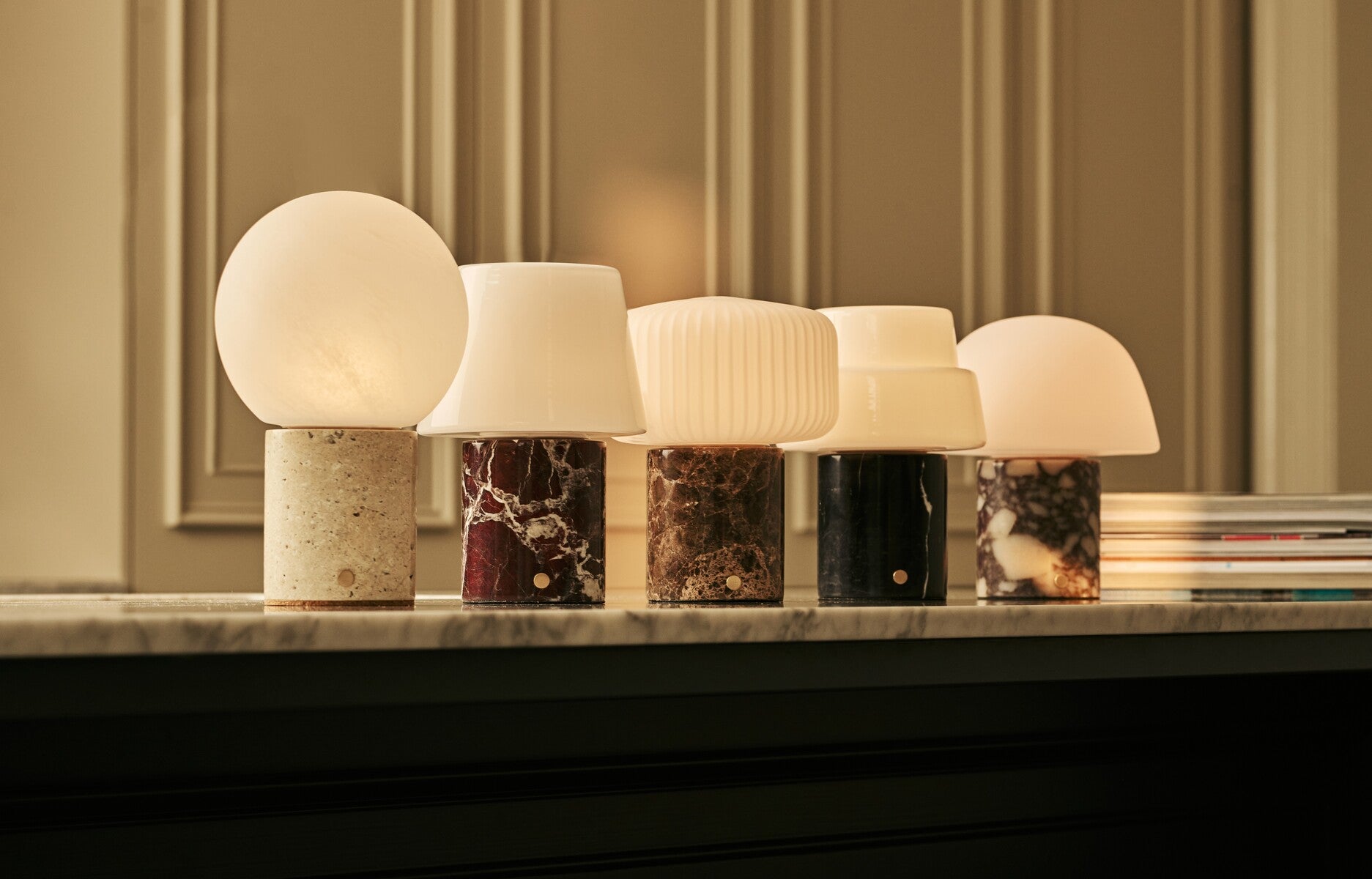 Tavellio Rijks collection of marble and stone table lamps glowing warmly in a row on a marble mantelpiece.