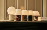 Tavellio Rijks collection of marble and stone table lamps glowing warmly in a row on a marble mantelpiece.