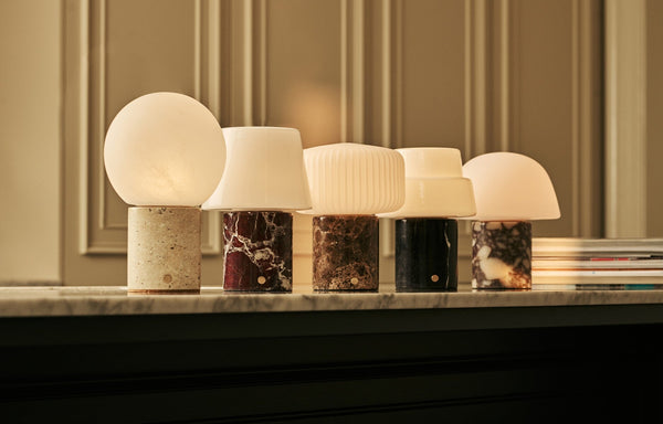 Tavellio Rijks collection of marble and stone table lamps glowing warmly in a row on a marble mantelpiece.