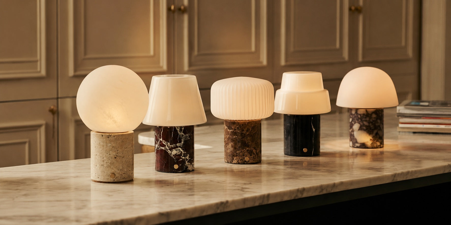 Tavellio, five marble table lamps with different colored shades lined up on a veined white marble countertop.