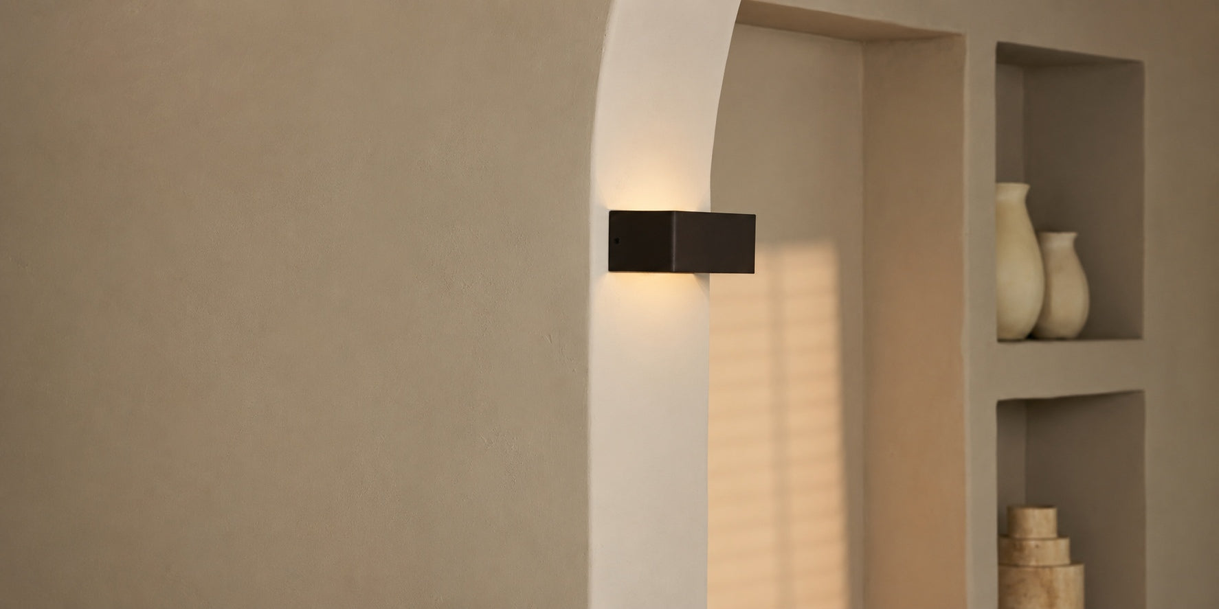 Tavellio black rectangular wireless wall lamp mounted on an archway beside a niche filled with vases.
