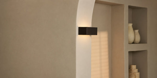 Tavellio black rectangular wireless wall lamp mounted on an archway beside a niche filled with vases.