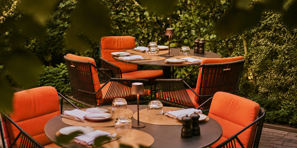 Tavellio small wireless table lamps softly lighting restaurant terrace tables surrounded by lush green hedges.