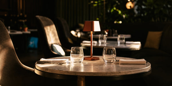 Tavellio terracotta wireless table lamp glowing on a marble bistro table set with sparkling water glasses.