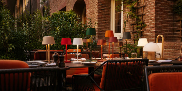 Tavellio, a row of colorful wireless table lamps glowing on a restaurant terrace table as evening falls.