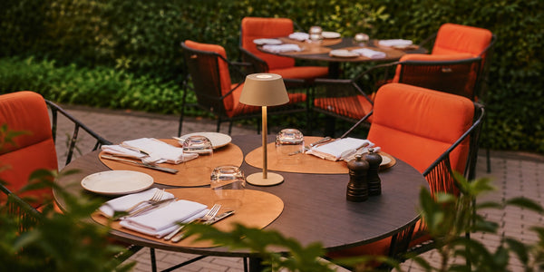 Tavellio beige wireless table lamp on a set restaurant terrace table, surrounded by orange armchairs.