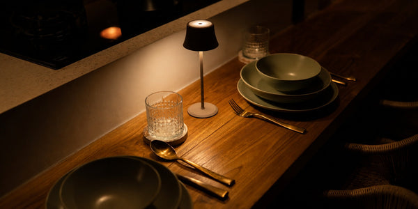 Tavellio black wireless table lamp glowing on a set hotel or restaurant table in a dim evening ambiance.