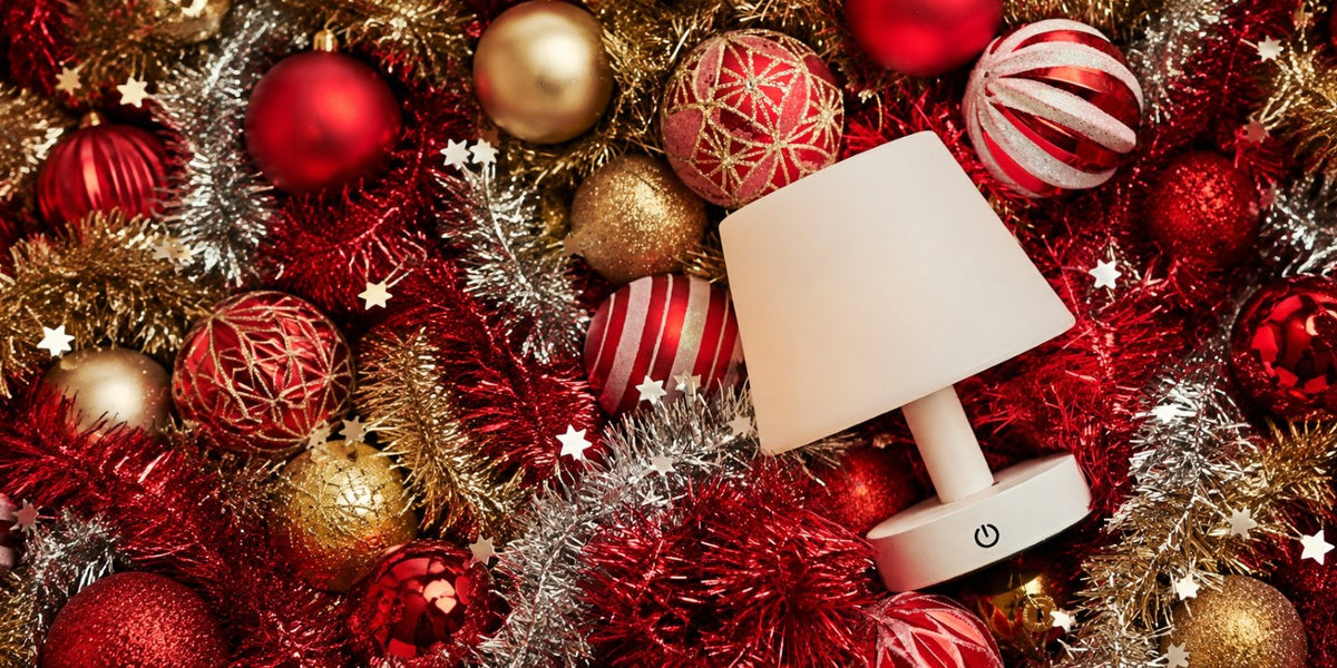 Rechargeable table lamp among red and gold Christmas baubles and tinsel as a festive gift
