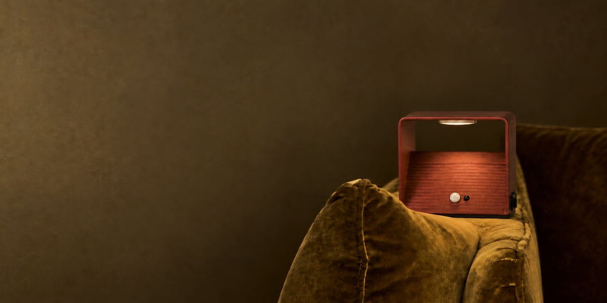 Rechargeable wall lamp with motion sensor glowing warm on a velvet sofa armrest