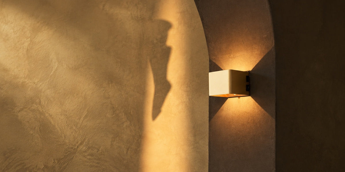 Square Tess rechargeable wall light glowing warm in a stone archway, seen up close