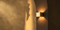 Square Tess rechargeable wall light glowing warm in a stone archway, seen up close