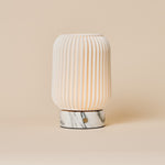 Cordless table lamp Alba with ribbed porcelain shade and Arabescato marble base on a plain backdrop