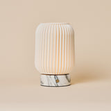 Cordless table lamp Alba with ribbed porcelain shade and Arabescato marble base on a plain backdrop