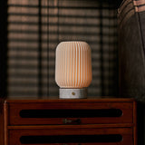 Alba cordless table lamp in Bianco Statuarietto white marble and porcelain lighting a striped-blind bedroom