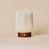 Rechargeable table lamp Alba in chestnut brown wood with fluted porcelain shade on a beige backdrop