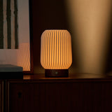 Cordless table lamp Alba in chestnut brown wood glowing warmly beside a framed botanical print