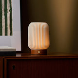 Tavellio Alba chestnut rechargeable table lamp lit on a wooden sideboard with mirror reflection