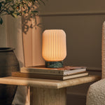 Tavellio Alba rechargeable table lamp lit atop stacked books on a travertine side table
