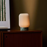 Alba cordless table lamp glowing on a wood sideboard against an olive green wall