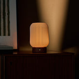 Tavellio Alba cordless table lamp in red travertine and porcelain, glowing warm on a dark wood sideboard at dusk