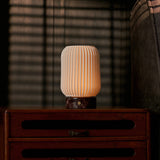 Alba rechargeable table lamp in Rosso Levanto marble and porcelain lighting a dim striped-blind bedroom