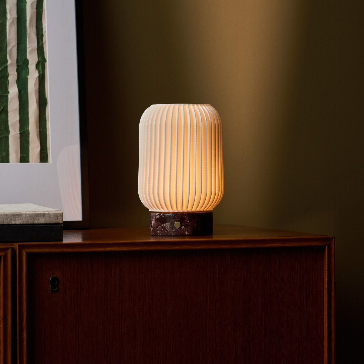 Tavellio Alba rechargeable table lamp with Rosso Levanto marble base glowing on a walnut sideboard