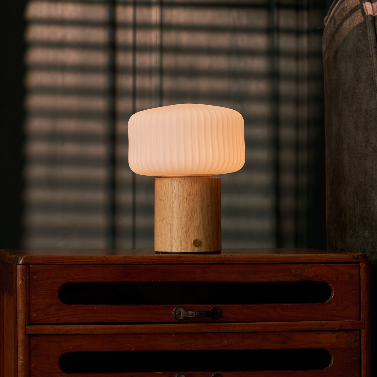 Andrew bois clair lampe de table rechargeable Tavellio – devant des stores vénitiens, près d'un fauteuil à rayures roses