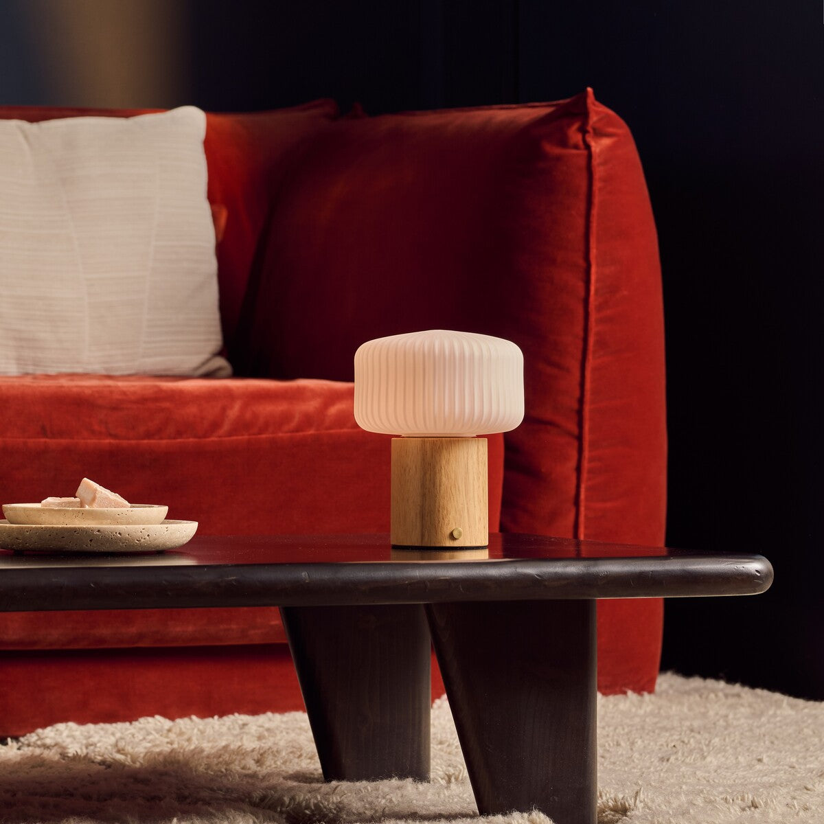 Andrew bois clair lampe de table rechargeable Tavellio – table basse noire devant un canapé en velours rouge – coupelle en travertin