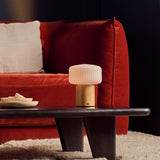 Andrew bois clair lampe de table rechargeable Tavellio – table basse noire devant un canapé en velours rouge – coupelle en travertin