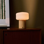Andrew bois clair lampe de table sans fil Tavellio – buffet en bois foncé devant un mur olive, abat-jour cannelé visible en gros plan