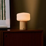 Andrew bois clair lampe de table sans fil Tavellio – buffet en bois foncé devant un mur olive, abat-jour cannelé visible en gros plan