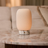 Tafellamp oplaadbaar Aurora Arabescato marmer en porselein, brandend op een marmeren tafel naast een beige bank