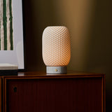 Aurora rechargeable table lamp with textured porcelain shade lit atop a sideboard against an olive-green wall