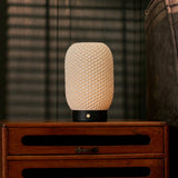Cordless table lamp Aurora in black wood and porcelain, glowing softly on a vintage wooden nightstand