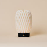 Rechargeable table lamp Aurora with black wooden base and woven porcelain shade on a beige backdrop