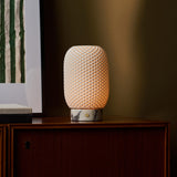 Cordless table lamp Aurora in Calacatta Vionaro marble and porcelain casting warm light reflected in a nearby picture frame