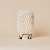 Cordless table lamp Aurora in Calacatta Vionaro marble and porcelain glowing on a wooden dresser beside a sofa