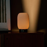 Aurora rechargeable table lamp glowing warmly in a dim room beside a framed textile print