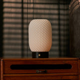 Aurora cordless table lamp lit atop a dark wood dresser with striped blind-cast shadows