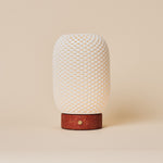 Cordless table lamp Aurora in Red Travertine and porcelain glowing on a wooden dresser beside a sofa