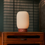 Rechargeable table lamp Aurora in Red Travertine and porcelain lit on a wood credenza beside framed wall art