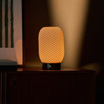 Aurora cordless table lamp casting a soft warm glow in a shadowy room near framed wall art