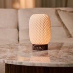 Tavellio Aurora cordless table lamp glowing on a marble side table beside a beige sofa and cushion