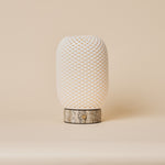 Rechargeable table lamp, Aurora Silver Travertine and Porcelain design, glowing beside framed art on a walnut sideboard