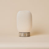 Rechargeable table lamp, Aurora Silver Travertine and Porcelain design, glowing beside framed art on a walnut sideboard