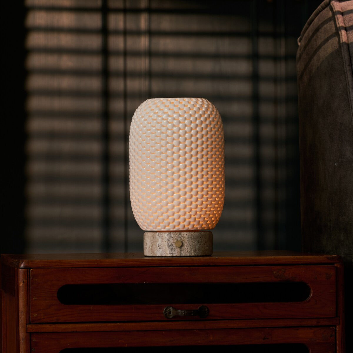 Tavellio rechargeable table lamp, Aurora Silver Travertine and Porcelain design, glowing on a wooden nightstand by blinds