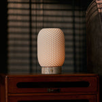 Tavellio rechargeable table lamp, Aurora Silver Travertine and Porcelain design, glowing on a wooden nightstand by blinds