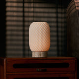Tavellio rechargeable table lamp, Aurora Silver Travertine and Porcelain design, glowing on a wooden nightstand by blinds
