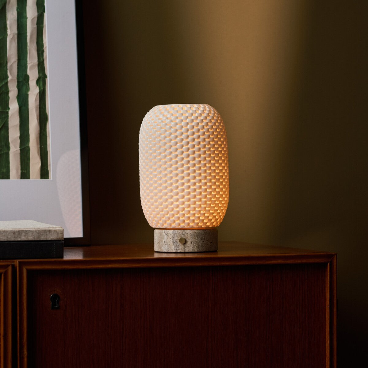 Cordless table lamp, Aurora Silver Travertine and Porcelain design, glowing on a beige studio backdrop